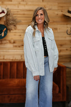 Load image into Gallery viewer, A woman modeling a light blue and white vertically striped button-down shirt over a black top and wide-leg blue jeans, standing in front of a rustic wood-paneled wall.