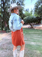 Load image into Gallery viewer, Woman wearing a denim jacket, orange skirt, and white boots outdoors.