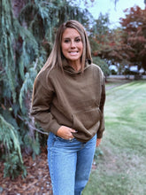 Load image into Gallery viewer, Woman wearing a brown hoodie and blue jeans standing outdoors with trees and grass in the background