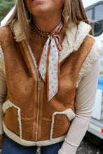 Load image into Gallery viewer, A close-up of a woman wearing a brown suede-like shearling vest with cream sherpa lining, a cream long-sleeve shirt underneath, and a patterned cream neck scarf.
